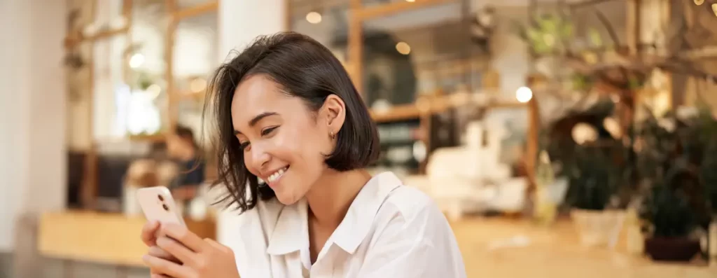 Woman smiling while looking at smartphone in cafe.