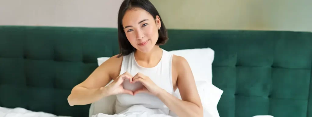 Woman making heart shape with hands in bedroom