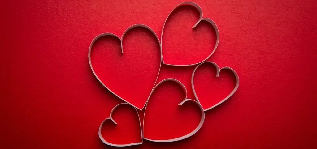 Paper hearts on red background for Valentine's Day.