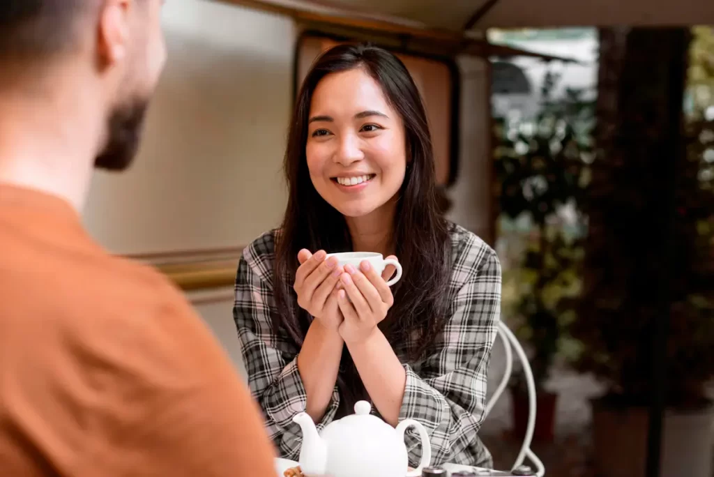 Mulher asiática a sorrir segurando uma chávena, num encontro casual de café.